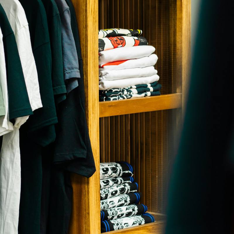 Folded T-shirts on wooden shelves beside hanging shirts