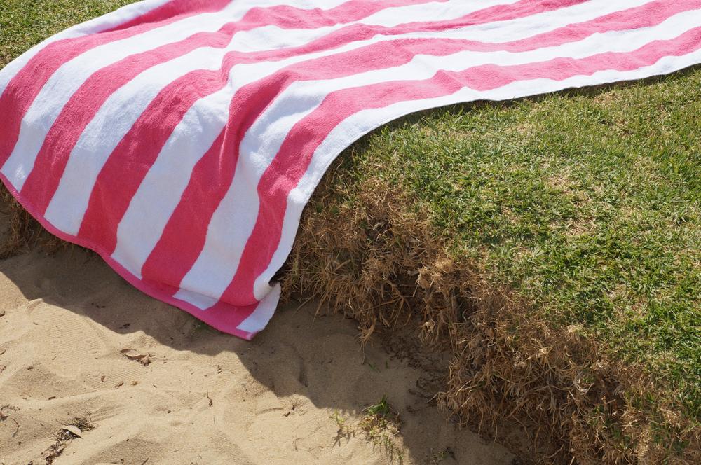 Pink and white striped cabana towel spread over grass and sand